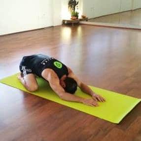 Man doing child's pose on a green yoga mat